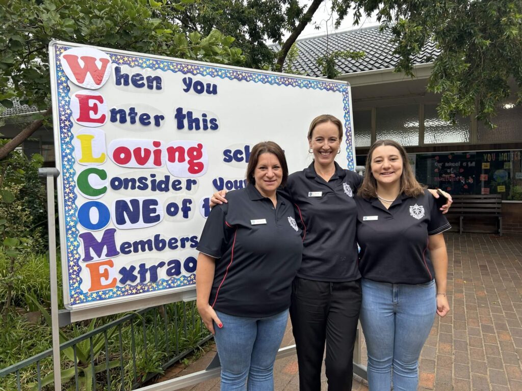 Three ladies posing in front of a sign board